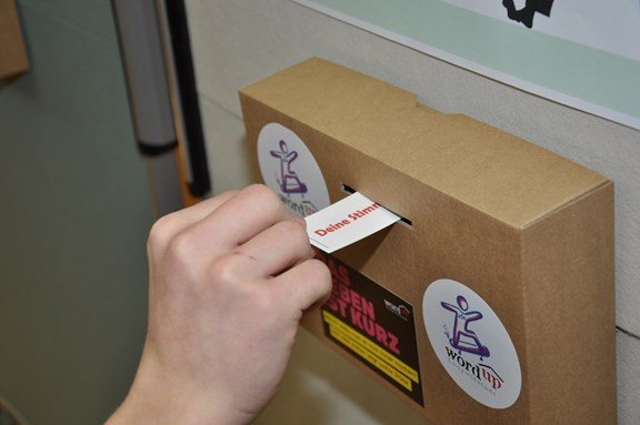Hand wirft Stimmzettel in Abstimmungsbox ein