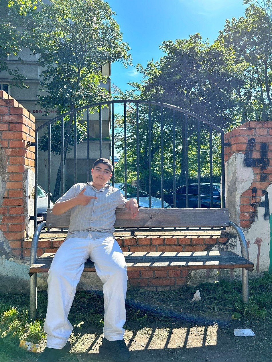 Jugendlicher Taha sitzt auf einer Parkbank und lächelt